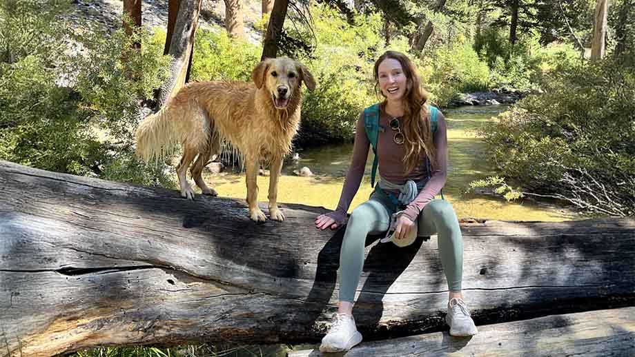 Kendra hiking with a dog resting on a fallen log in forest